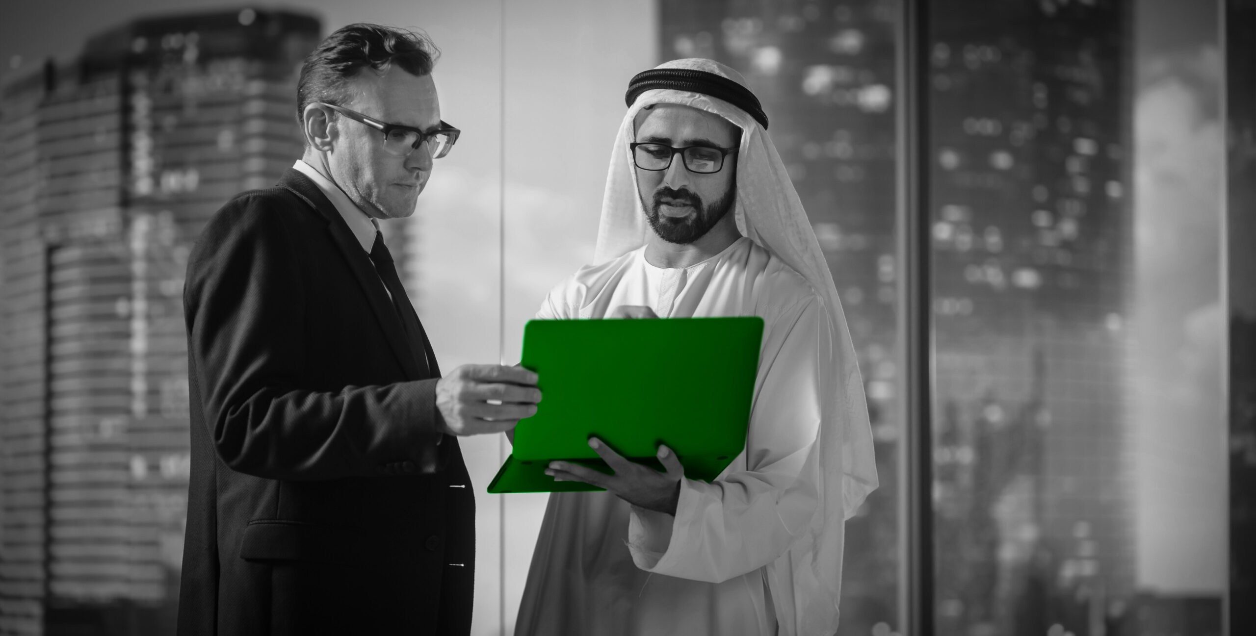 Businessmen reviewing a laptop against Dubai skyline, real estate partnership